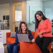 Digitale Zusammenarbeit mit Zoho Cliq ganze einfach, zwei Frauen sitzen auf einer Couch und schauen auf einen Laptop