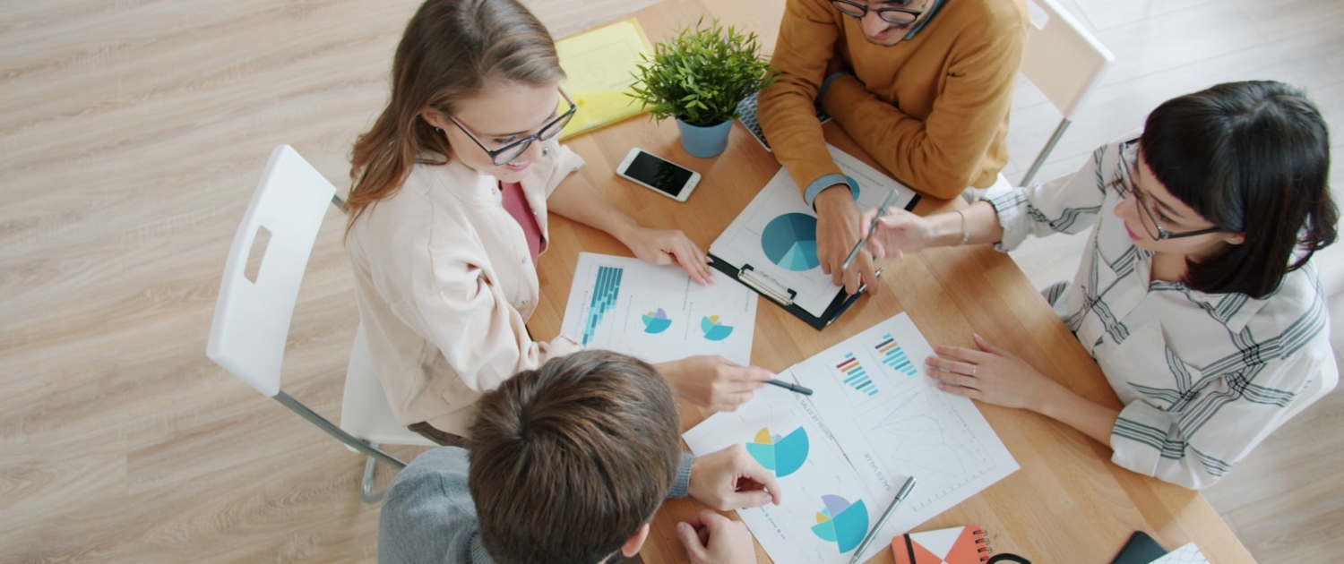 Four people collaborating around a table with charts.